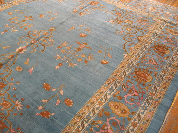 Close-up of a blue rug with intricate floral patterns in rust, gold, and pink, resting on hardwood floors.