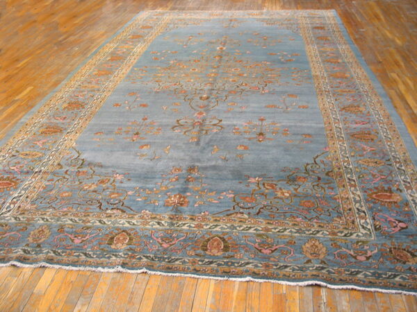 Dusty blue rug with detailed floral patterns in orange and pink covers wide plank wood flooring.