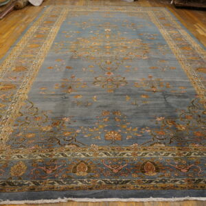 Ornate dusty blue rug with tan and gold floral patterns laid out on wood flooring.