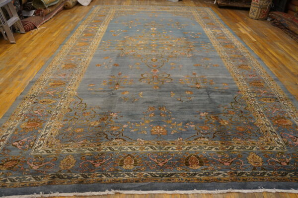 Ornate dusty blue rug with tan and gold floral patterns laid out on wood flooring.