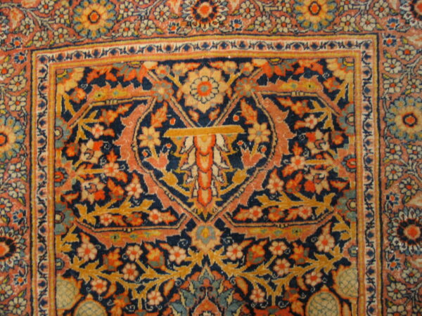 Close up of a woven rug showing a navy, coral, and gold floral medallion and a patterned border.