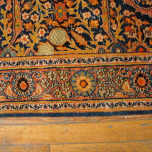 Ornate navy, gold, and terracotta floral rug with complex borders placed on light wood flooring.