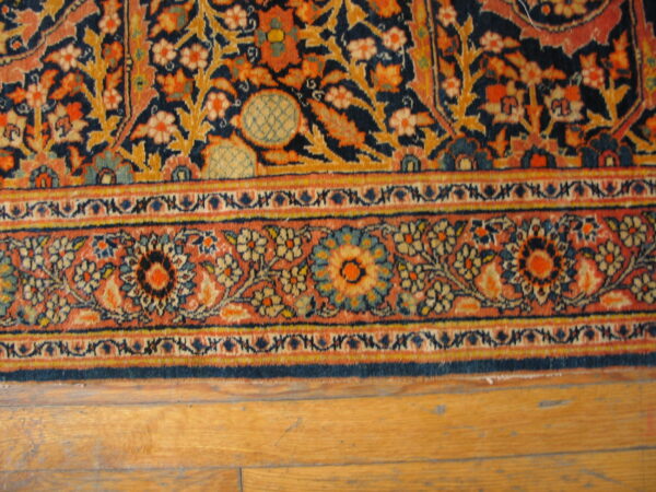 Ornate navy, gold, and terracotta floral rug with complex borders placed on light wood flooring.