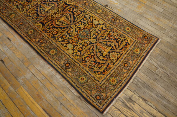 A low-pile rug with navy, gold, and orange floral patterns sits on rustic wood plank flooring.
