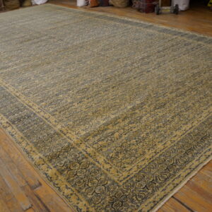 Low-pile tan and navy rug featuring an intricate floral pattern and multiple borders on rustic wood planks.