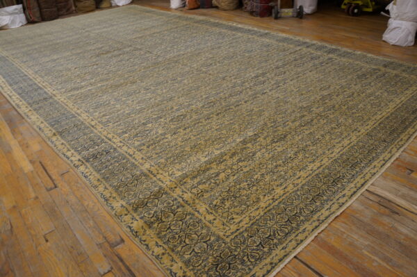 Low-pile tan and navy rug featuring an intricate floral pattern and multiple borders on rustic wood planks.
