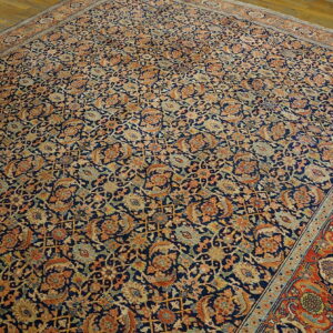 Large traditional rug with a dense navy, rust, and tan floral pattern lying on hardwood floors.