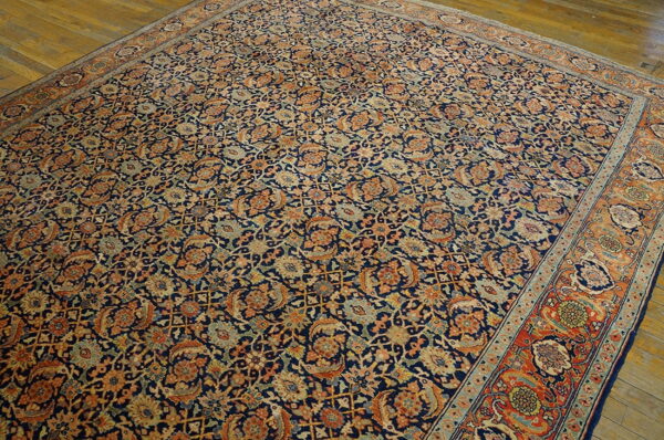 Large traditional rug with a dense navy, rust, and tan floral pattern lying on hardwood floors.