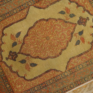 Low pile rug featuring a rust medallion on a golden tan field, framed by complex blue and green borders.
