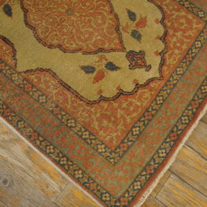 A low-pile rug with gold and terra cotta traditional patterns rests on rustic wooden planks.
