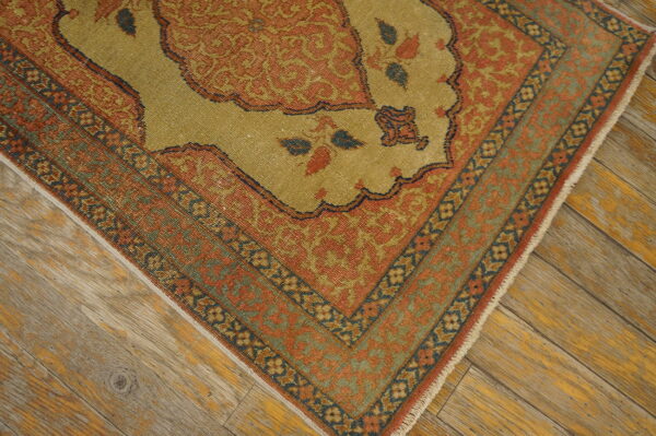 A low-pile rug with gold and terra cotta traditional patterns rests on rustic wooden planks.