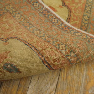 Muted orange and sage patterned rug, partially curled, showcasing low pile texture on rustic wooden floorboards.