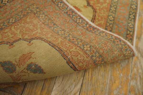 Muted orange and sage patterned rug, partially curled, showcasing low pile texture on rustic wooden floorboards.