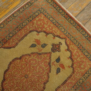 Tight-weave rug with a gold central field and rust borders featuring ornate patterns on distressed wood flooring.