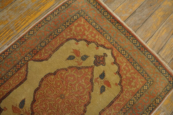 Tight-weave rug with a gold central field and rust borders featuring ornate patterns on distressed wood flooring.
