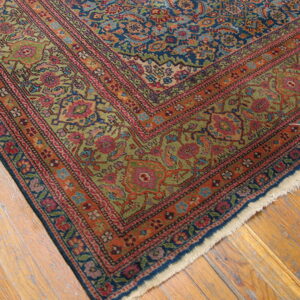 Close-up of a rug corner showing blue, red, orange, and green floral patterns on distressed wood flooring.