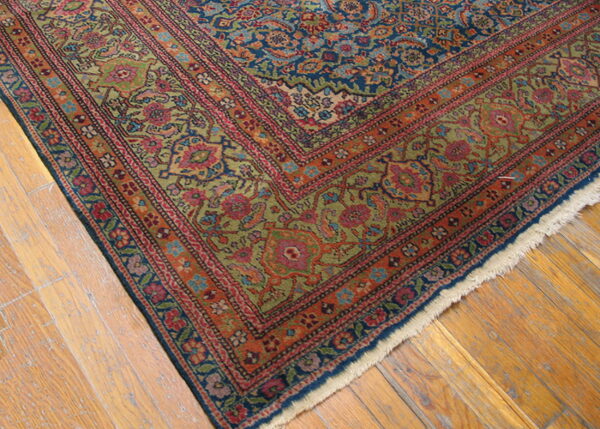 Close-up of a rug corner showing blue, red, orange, and green floral patterns on distressed wood flooring.