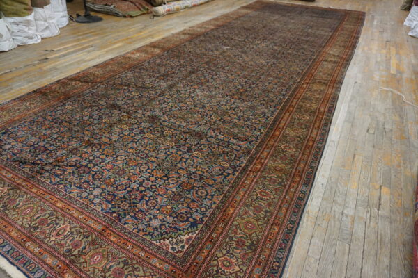 Large navy blue and rust area rug with dense traditional patterns covers distressed wooden flooring.
