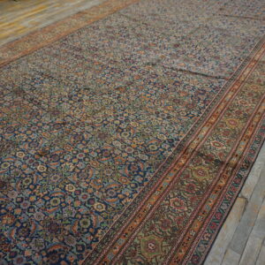 Long navy and multicolor patterned rug with wide borders rests on worn light gray wood floors.
