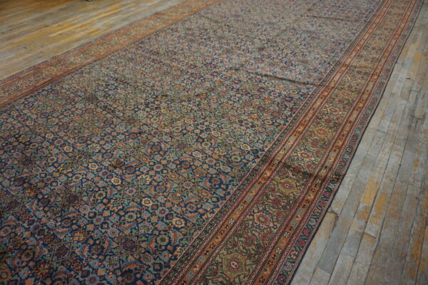 Long navy and multicolor patterned rug with wide borders rests on worn light gray wood floors.