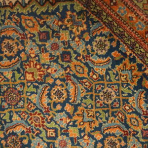 Intricate traditional rug pattern featuring orange, green, and burgundy details on a navy blue background, including a striped border.