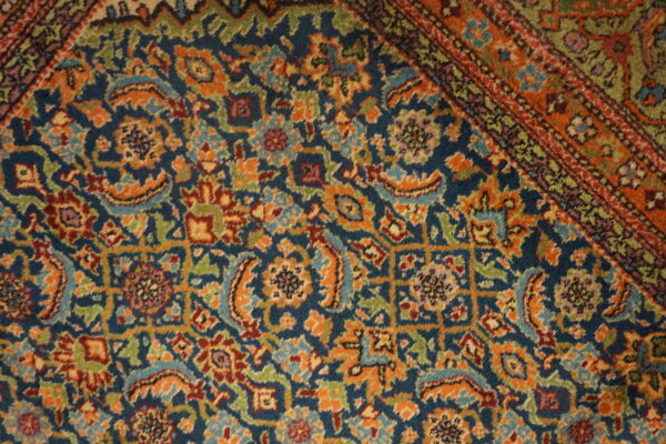 Intricate traditional rug pattern featuring orange, green, and burgundy details on a navy blue background, including a striped border.