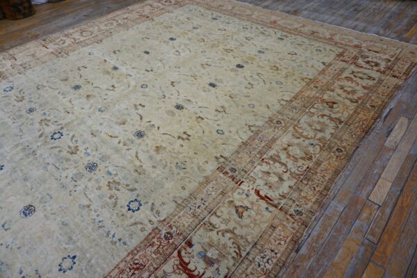 Ornate beige rug with brown, blue, and rust accents lying on rustic, wide-plank wood flooring.