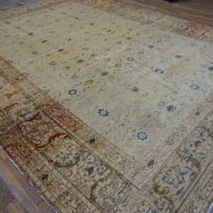 Low-pile beige traditional rug featuring blue and rust floral motifs on distressed wood planks.