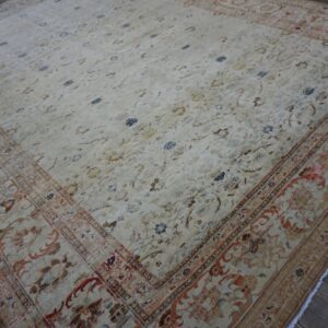 Ornate cream rug featuring muted patterns in rust and blue on dark, distressed plank flooring.
