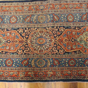 Ornate rug featuring floral motifs in terracotta, navy, and teal, resting on wood planks.