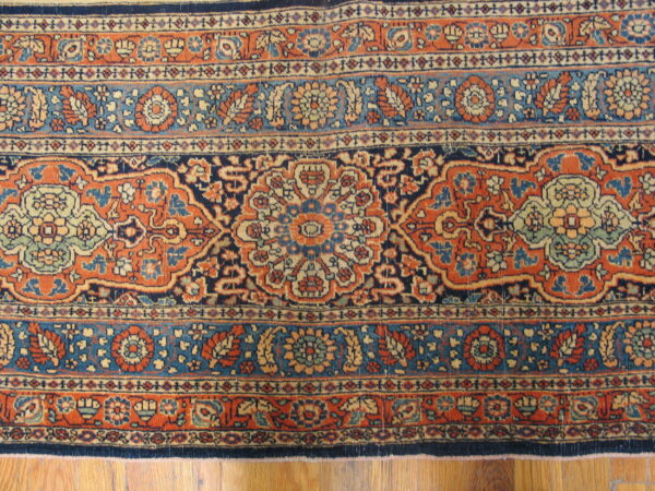 Ornate rug featuring floral motifs in terracotta, navy, and teal, resting on wood planks.