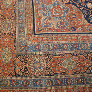 Ornate area rug corner detail showing complex floral medallions in navy blue, rust orange, and light blue.