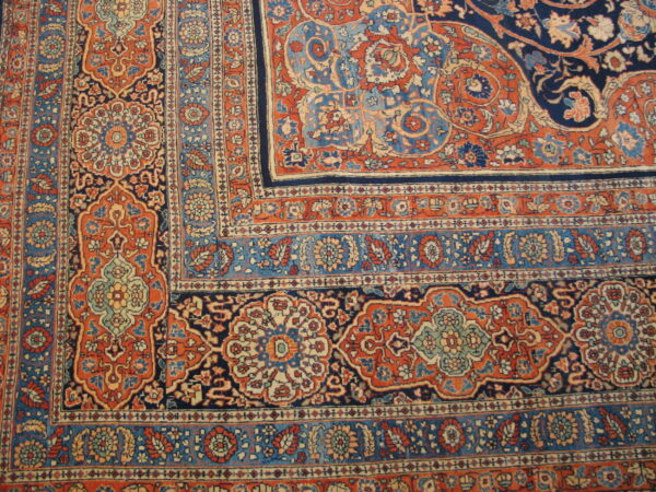 Ornate area rug corner detail showing complex floral medallions in navy blue, rust orange, and light blue.