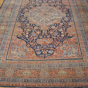 Traditional low-pile rug with complex floral patterns in deep blue, rust, and light blue on hardwood.