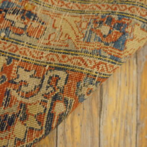 Tightly woven rug in distressed red, navy, and beige patterns rests on worn, light wood flooring.