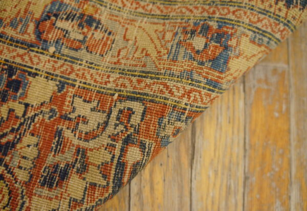 Tightly woven rug in distressed red, navy, and beige patterns rests on worn, light wood flooring.