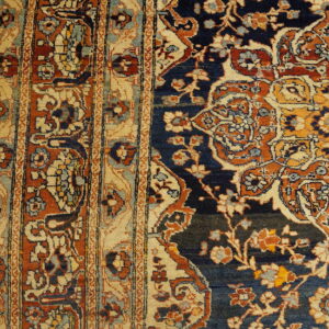 A rug border with beige and orange stripes meets a navy floral field on rustic hardwood planks.