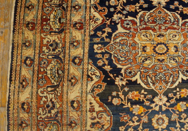 A rug border with beige and orange stripes meets a navy floral field on rustic hardwood planks.