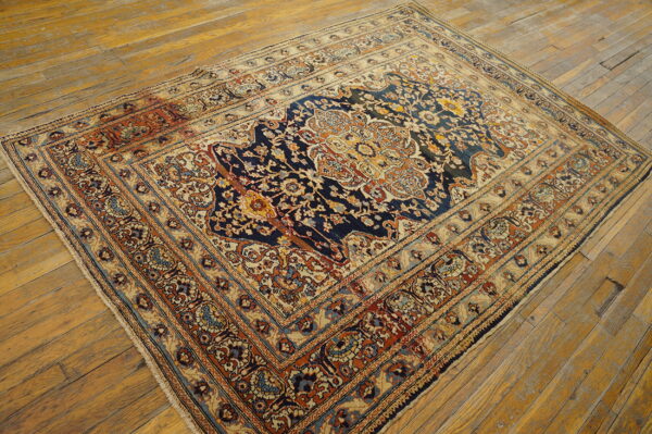 Traditional patterned rug in navy, cream, and rust colors on distressed light brown wooden floorboards.
