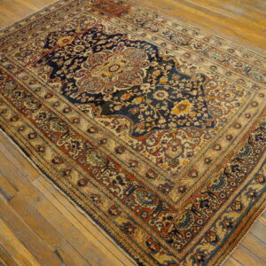 Traditional navy and beige low-pile rug with floral medallion sits on rustic golden-toned hardwood flooring.