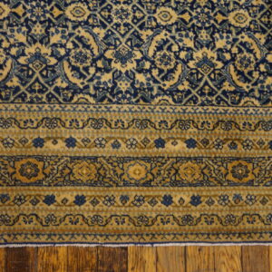 Navy blue and gold rug displaying dense field and striped floral borders on wooden plank flooring.