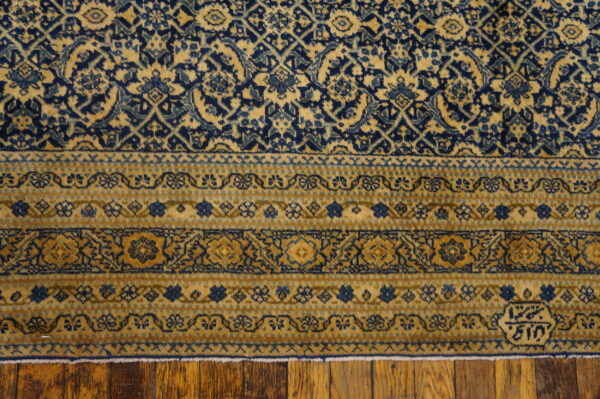 Navy blue and gold rug displaying dense field and striped floral borders on wooden plank flooring.