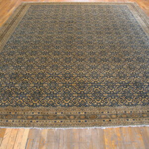 Large navy and gold patterned rug with wide decorative borders displayed on light brown hardwood flooring.