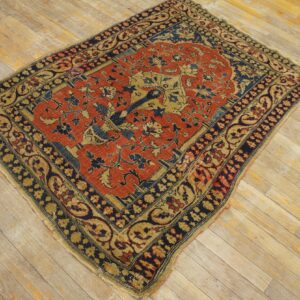 Rust and navy low pile rug with an intricate tree-of-life motif on distressed wood plank flooring.