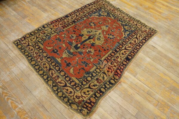 Rust and navy low pile rug with an intricate tree-of-life motif on distressed wood plank flooring.