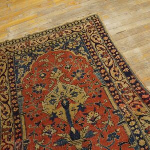 A low-pile traditional rug with red, navy, and tan floral patterns sits on distressed light wood.