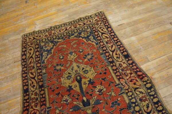 A low-pile traditional rug with red, navy, and tan floral patterns sits on distressed light wood.