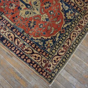 Close-up of a traditional red, navy, and tan floral rug corner on rustic gray wood planks.