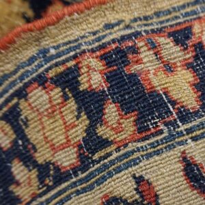 Close-up shows the low pile texture and geometric pattern in tan, navy, and red.