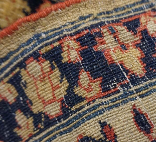 Close-up shows the low pile texture and geometric pattern in tan, navy, and red.